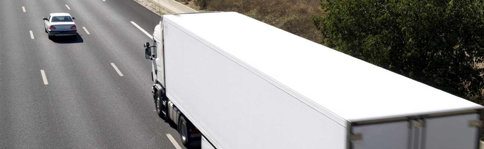 Weiße Lkw-Fahrzeug auf einer mehrspurigen Straße neben einem blauen Auto.